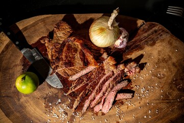 Sliced grilled steak with lime, onion, and garlic on a wooden board.