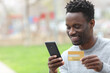 © PheelingsMedia - Happy black man buying online in the street