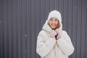 Wall Mural - A happy woman in knitted mittens poses against a background of a gray wall in winter