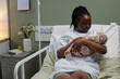 © pressmaster - Caring mother holding newborn baby while sitting on hospital bed in maternity ward gently looking at baby with affection and tenderness mother filled with emotion