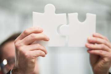 Portrait of optimistic bearded businessman holding puzzle pieces, solving tasks, looking at camera