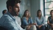 © VK Studio - A man in a blue shirt speaks intently in a formal meeting, with several people attentively listening in a brightly lit room.