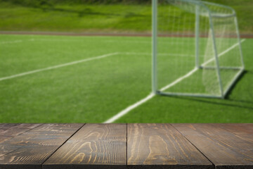 Empty wood table top with blurred outdoors football goal or soccer field. Abstract background. Mock up for montage product display or design your products.