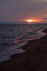 Poster - The sun sets on the horizon, casting golden hues over gentle waves lapping against the sandy beach