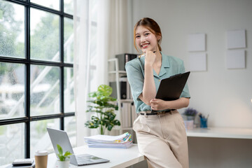 Wall Mural - A woman is standing in front of a window with a laptop and a clipboard