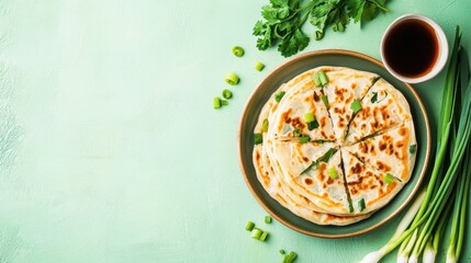 A plate of sliced scallion pancakes with dipping sauce and fresh herbs on a pastel background.