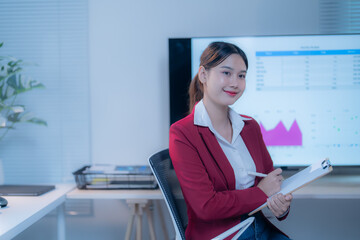 Young asian businesswoman confidently takes notes in a modern office during a successful meeting, showing leadership and professionalism