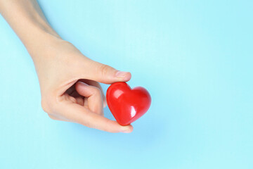 Wall Mural - Woman holding red heart on light blue background, top view