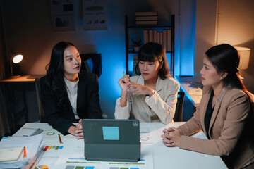 Wall Mural - Three asian businesswomen having a late night meeting in the office, using a tablet and going over paperwork