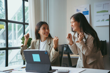 Two happy businesswomen are celebrating a success while looking at a tablet computer in a modern office