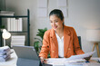 © amnaj - Young asian businesswoman is working at her desk in the office, smiling as she uses her tablet computer to go over paperwork