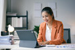 © amnaj - Asian businesswoman is smiling while working on a tablet at her desk in her bright and modern office