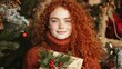 © Maria Starus - A girl with red hair holding a present in front of a christmas tree