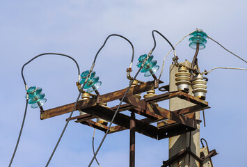 An old and rusty power transmission line with disk insulators made of hardened glass against blue sky