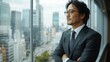 © Ami - フォーマルなスーツを着た日本人ビジネスマンが、企業情報を得るために都会の街並みを眺めている