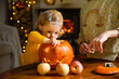 © Suzi Media  - Father his toddler and daughter carving pumpkin jack o lantern, Halloween celebration at home. Fun craft and decoration at home. Happy children and their dad preparing for the holiday, decorating the