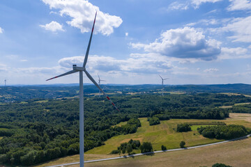 Aerial view of wind turbines in a green landscape under a blue sky with fluffy clouds. The scene captures renewable energy and the beauty of nature.