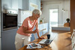 © Marko Geber - Senior woman managing finances on laptop at home