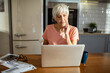 © Marko Geber - Senior woman managing finances on laptop at home