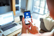 © Marko Geber - Senior woman checking bank account on smartphone with laptop in the background at home