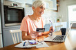 © Marko Geber - Senior woman shopping online with credit card and laptop at home