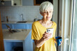 © Marko Geber - Elderly woman using smartphone in modern kitchen
