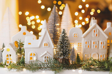 Wall Mural - Christmas little ceramic houses, trees and lights on dark background with golden bokeh in eve. Merry Christmas! Atmospheric Christmas scene, miniature holiday village. Xmas background