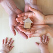 © Michael - Baby hands lie net to a tiny wooden house that is placed in the open hands of its parents.