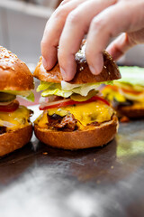 Wall Mural - Close-up of a hand placing the top bun on a cheeseburger with lettuce, tomato, and melted cheese. Perfect for food blogs, menus, or culinary articles.