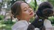 © stockbusters - Affectionate girl kissing poodle in park closeup. Joyful woman cuddling puppy
