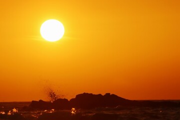 Ocean waves fighting with rocks and orange sky with sunset