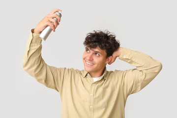 Canvas Print - Handsome young man applying hair spray on his curly hair against grey background