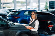 © Zamrznuti tonovi - Elegant businesswoman surveys cars holding a book of notes