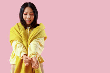 Canvas Print - Young Asian woman in yellow hoodie with scarf on pink background