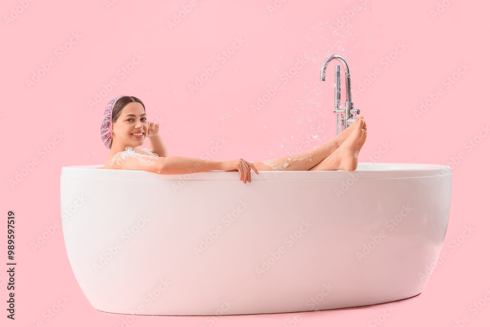 Young woman taking bath on pink background