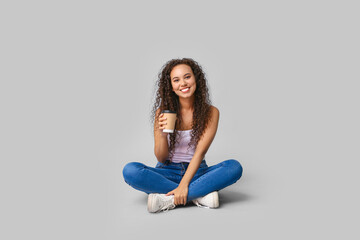 Poster - Happy young African-American woman with paper cup of coffee sitting on white background