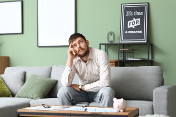 Wall Mural - Thoughtful young man in debt sitting on sofa at home