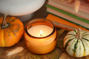 Wall Mural - Burning candle, pumpkins and stack of books on wooden table, closeup. Autumn atmosphere