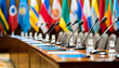 © Eddy Drmwn - A row of microphones on a conference table with blurred flags in the background.