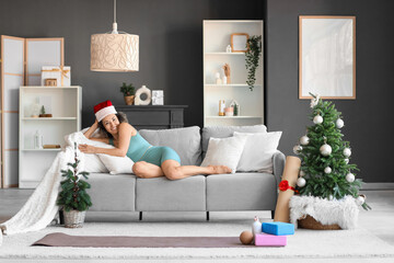 Sporty mature woman in Santa hat lying at home on Christmas eve