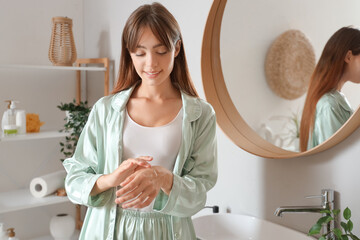 Poster - Morning of young woman applying cream onto her hand in bathroom