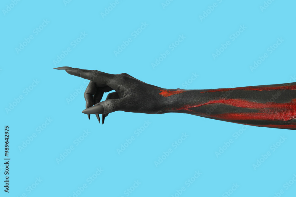 Black witch hand with claws pointing at something on blue background. Halloween celebration