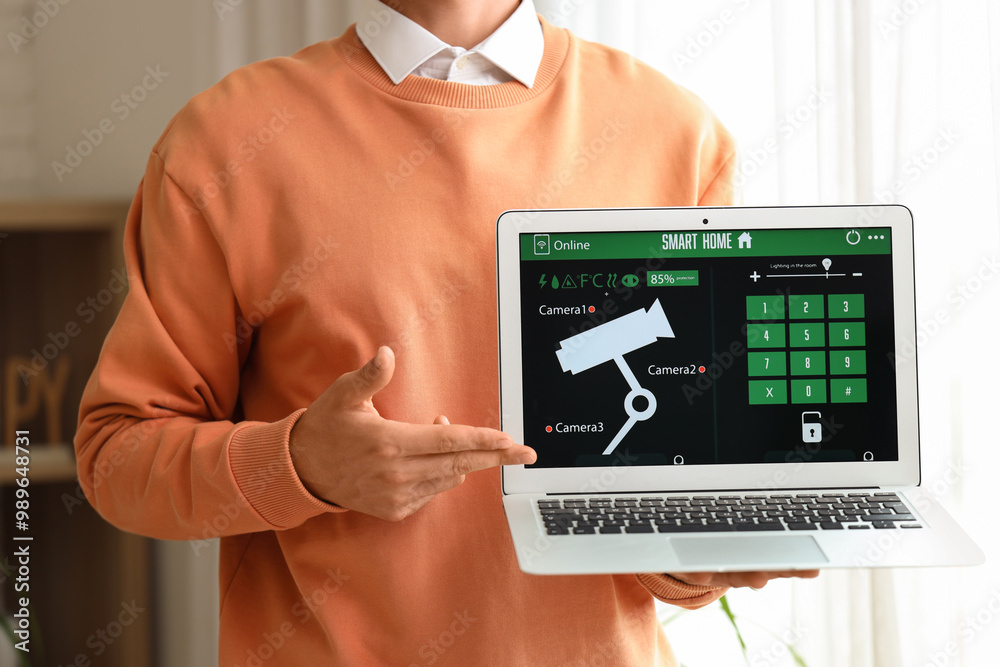Young man using laptop with smart home security system application in room, closeup