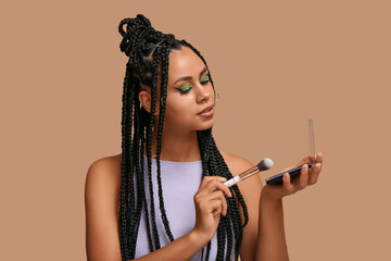 Poster - Young African-American woman with braids and beautiful makeup holding palette of eyeshadows and brush on brown background