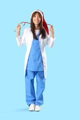 Poster - Female Asian doctor in Santa hat with stethoscope on blue background