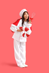 Poster - Female Asian chef with gift whisk and candy cane pillow on red background. Christmas celebration