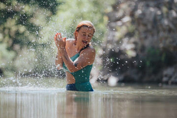 Wall Mural - A joyful woman splashes water while swimming in a serene natural setting. The scene captures the feeling of joy, relaxation, and connection with nature.