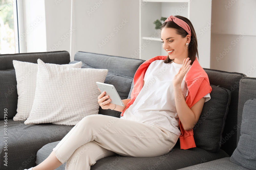 Young woman with tablet computer video chatting on sofa at home