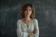 © Studium L&M - Serious teacher standing in front of a chalkboard with arms crossed in a classroom setting