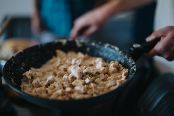 Close-up of a person preparing a delicious creamy chicken dish in a frying pan. The kitchen scene conveys warmth and the joy of home-cooked meals.